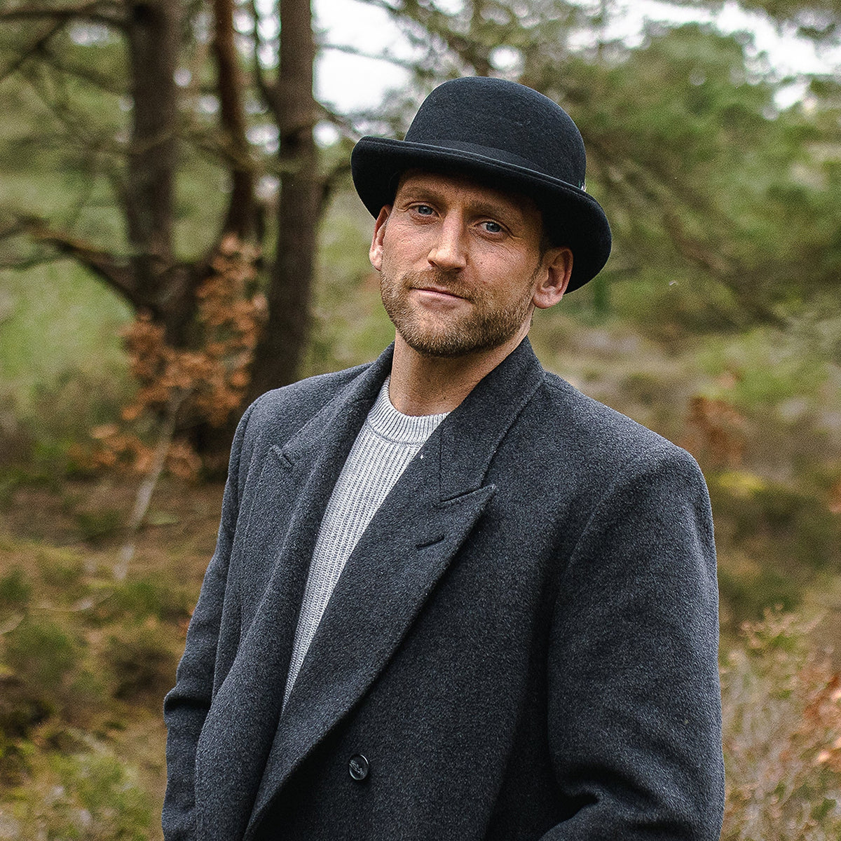 Black bowler hat with curved brim, band and colourful feather detail