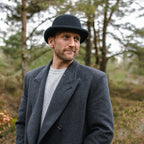 Black bowler hat with curved brim, band and colourful feather detail