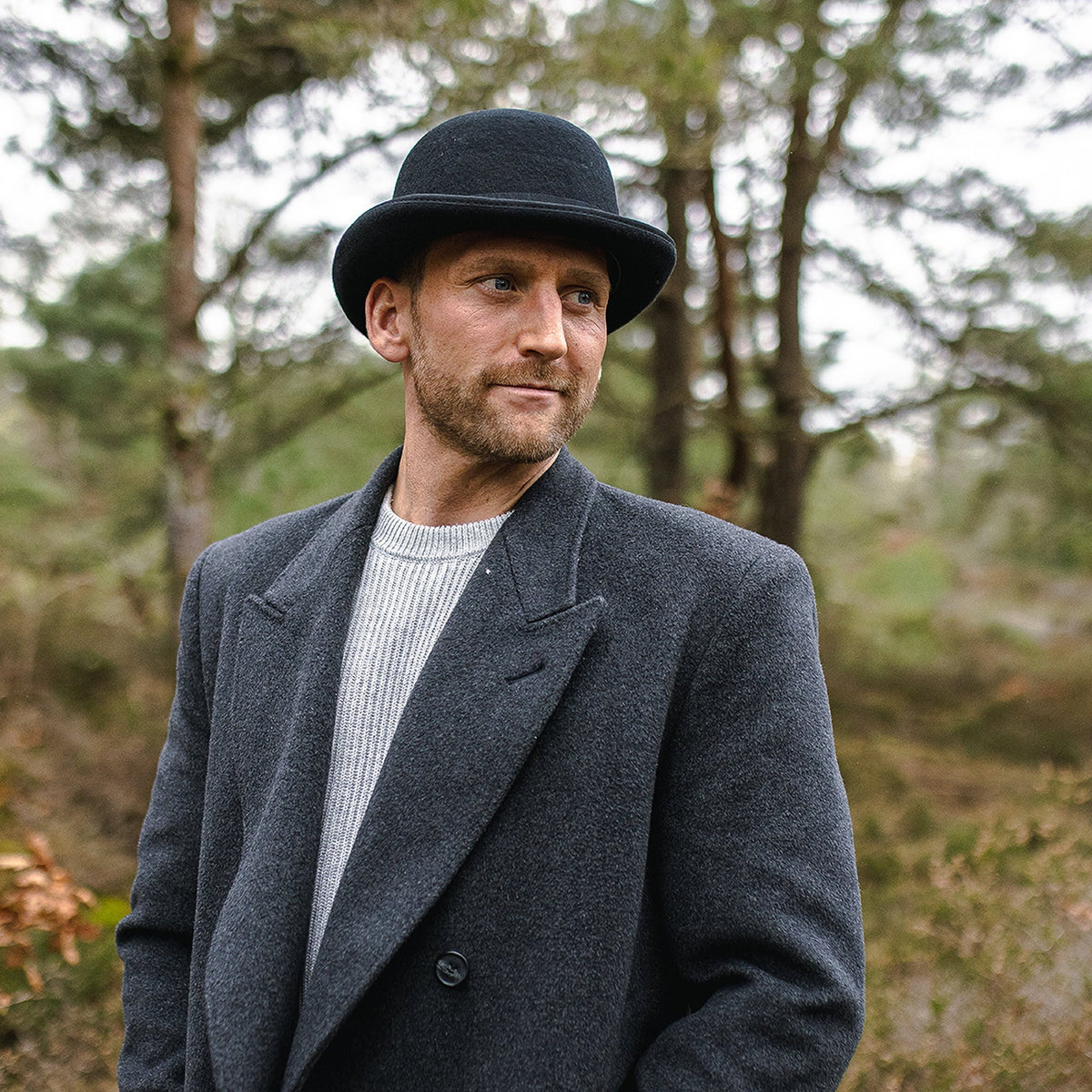 Black bowler hat with curved brim, band and colourful feather detail