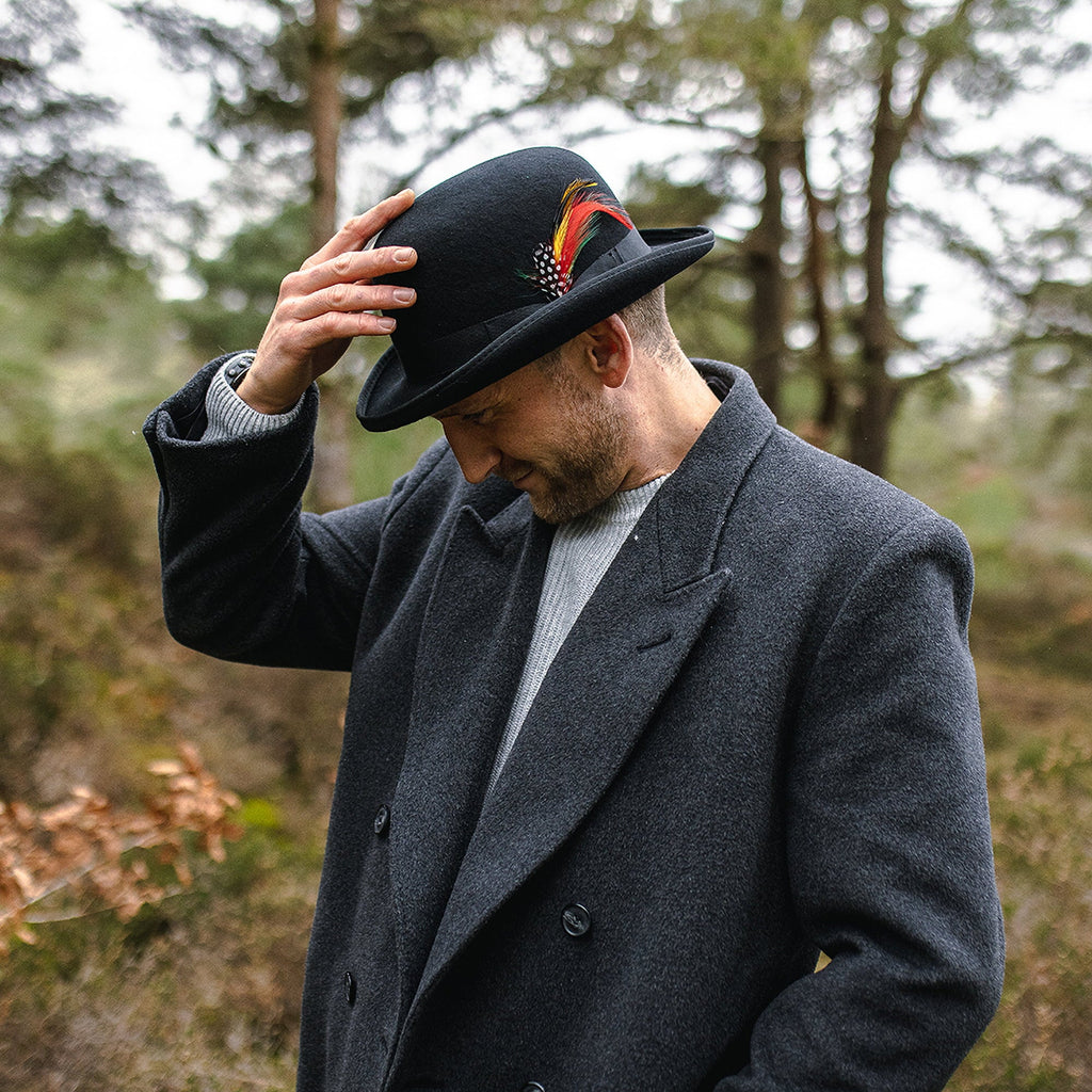 Black bowler hat with curved brim, band and colourful feather detail