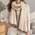 Women's cream knitted shawl scarf with contrasting border draped around the neck