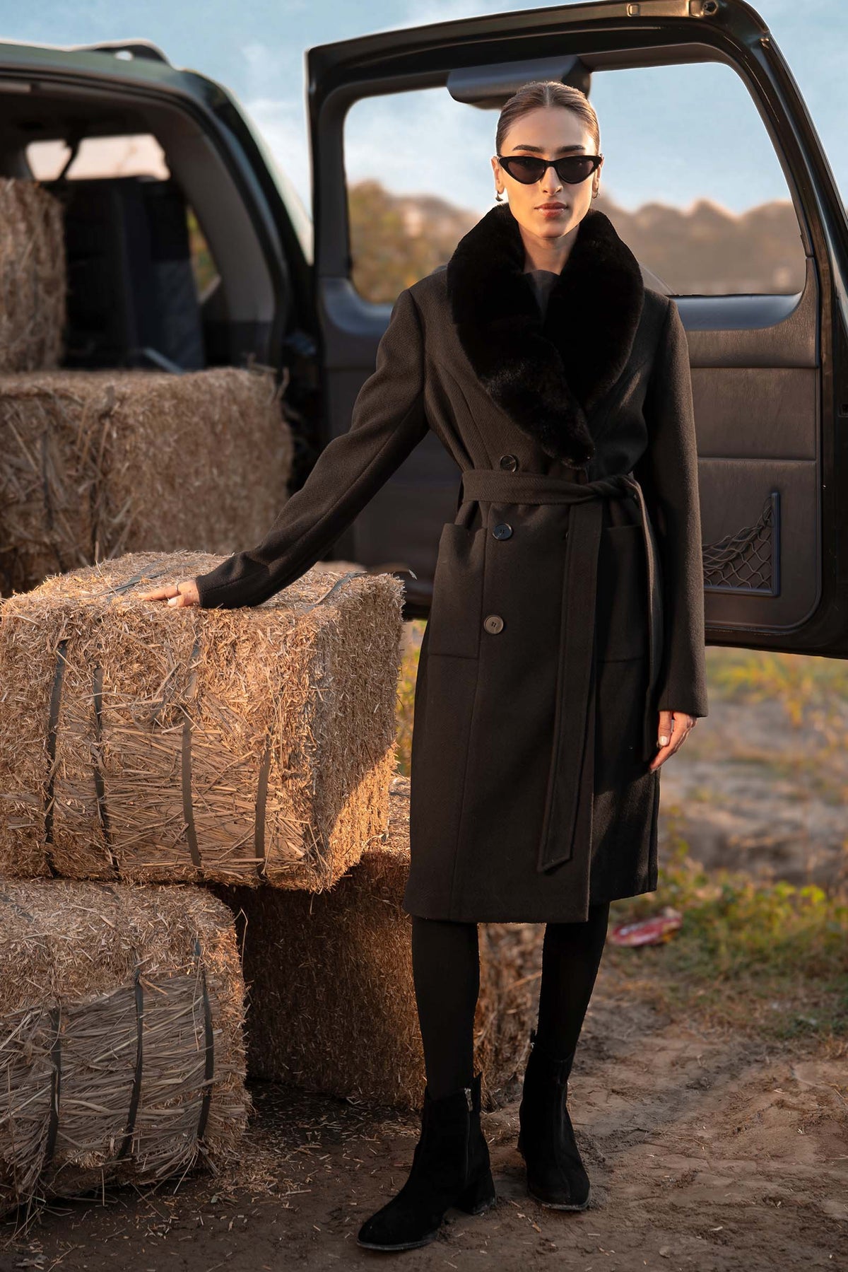 Woman wearing a black belted long coat with a wide plush-look collar
