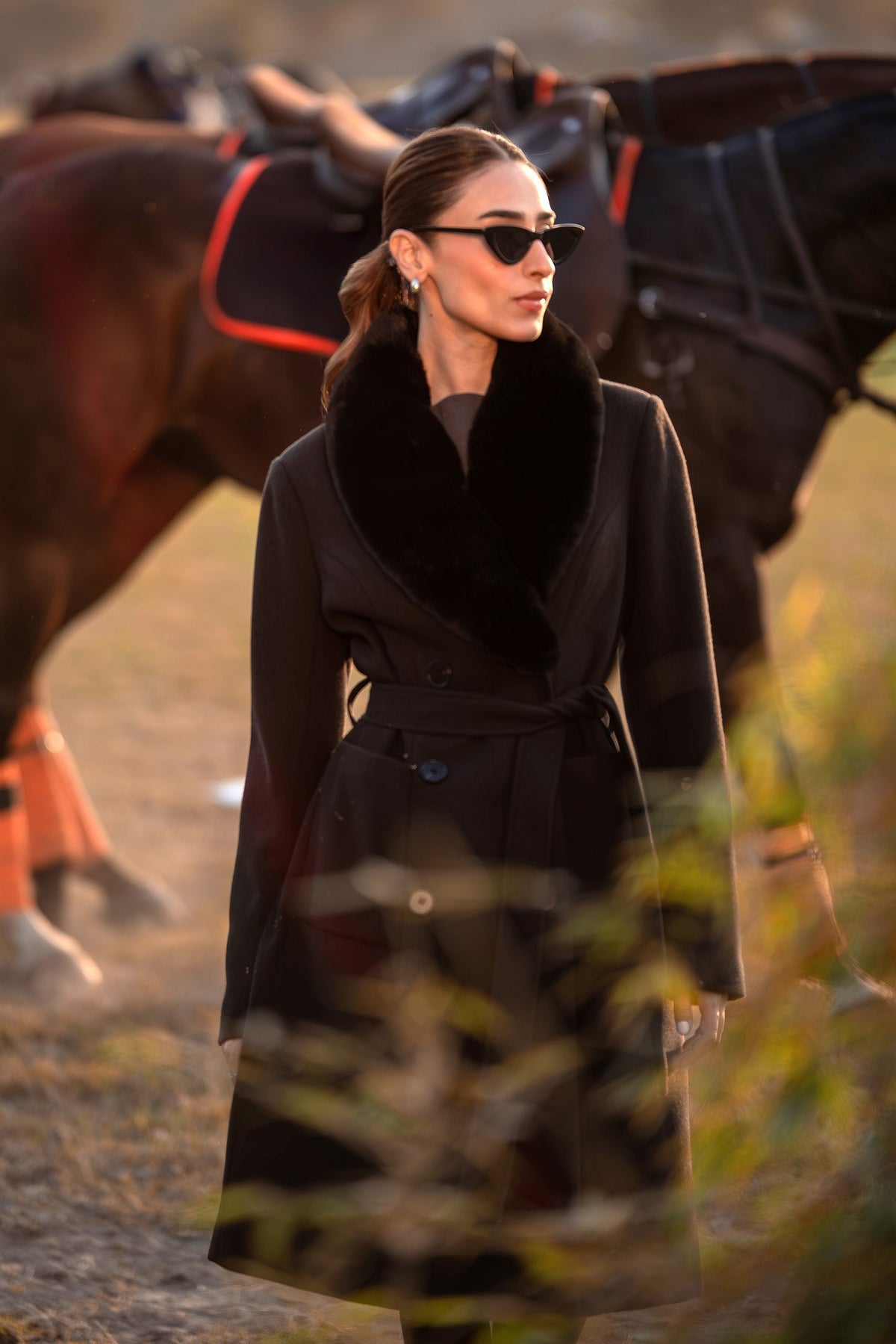 Woman wearing a black belted long coat with a wide plush-look collar