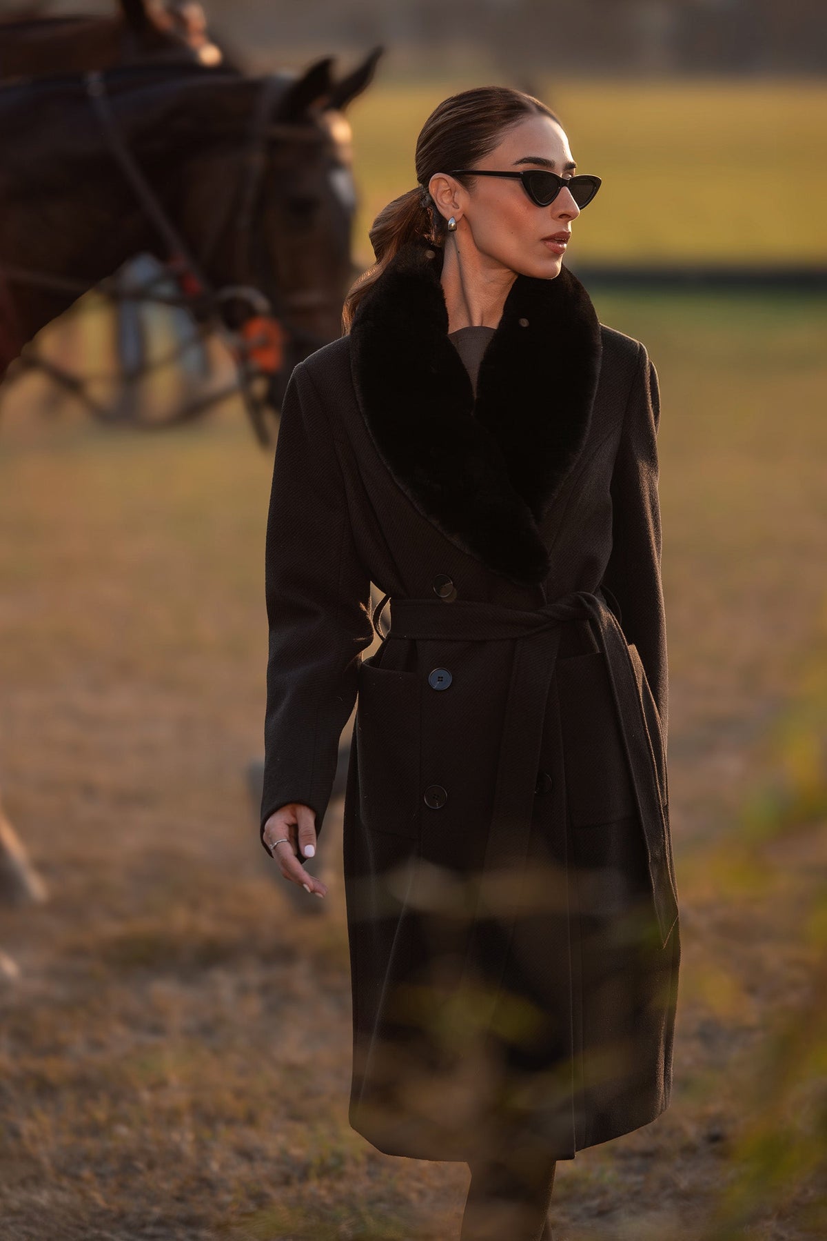 Woman wearing a black belted long coat with a wide plush-look collar