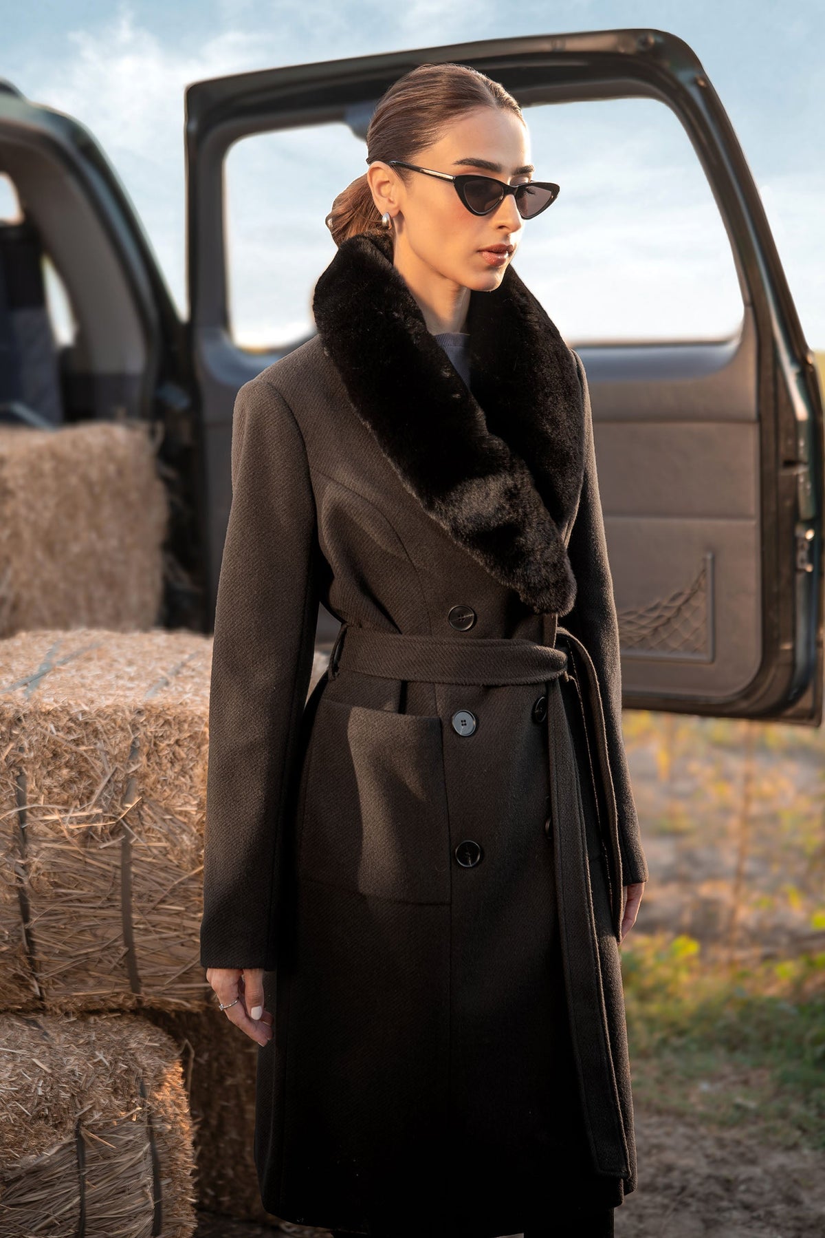 Woman wearing a black belted long coat with a wide plush-look collar