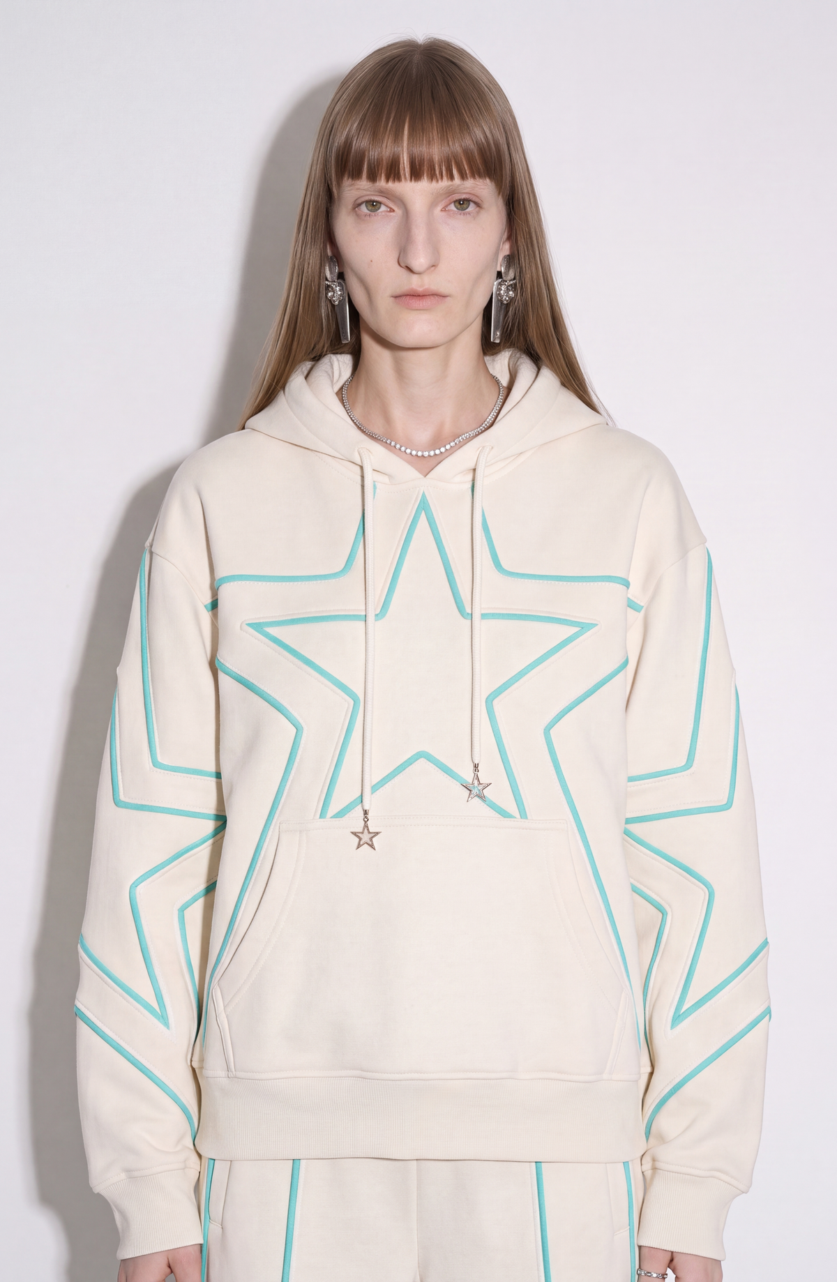 Cream hoodie with turquoise outlined star motifs, drawstring hood and front kangaroo pocket